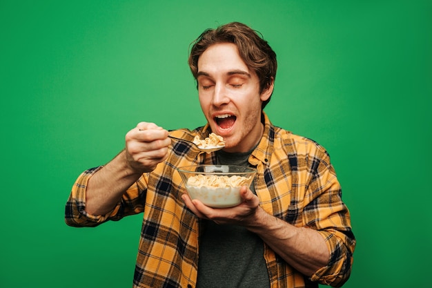 Jonge man eet vlokken met melk en ziet er gelukkig uit