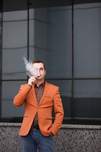 Jonge man elektronische sigaret roken op de achtergrond van het gebouw.