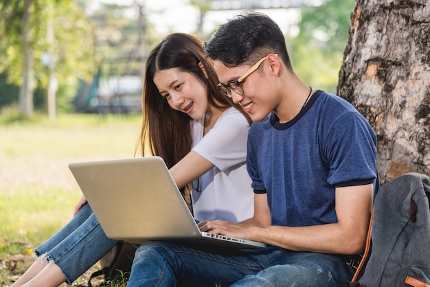 Jonge man en meisjesvriend klasgenoten die in het park onder boom zitten, overleggen samen op laptop op de universiteit