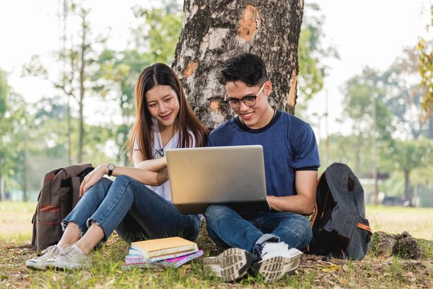 Jonge man en meisjesvrienden die onder een boom zitten, overleggen samen op een laptop op de universiteit
