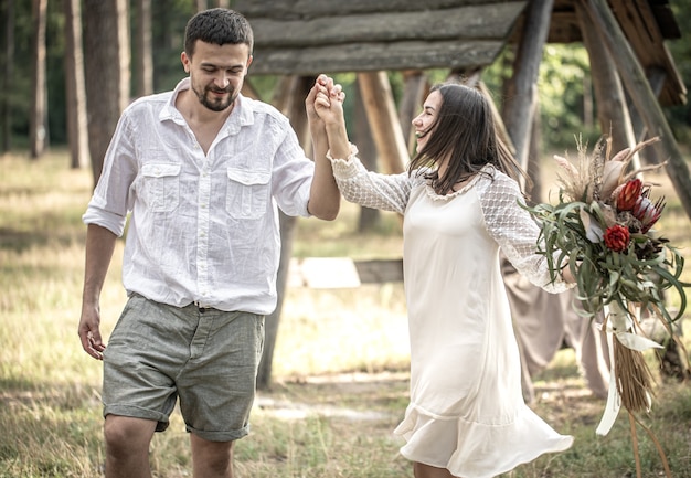 Jonge man en vrouw netjes gekleed, met een boeket exotische bloemen lopen in het bos, op een date in de natuur.