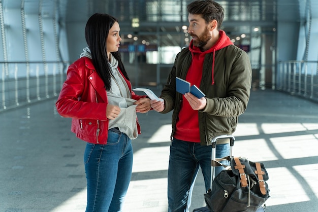 Jonge man en vrouw ruzie met elkaar terwijl ze kaartjes vasthouden en op de luchthaven staan. problemen concept