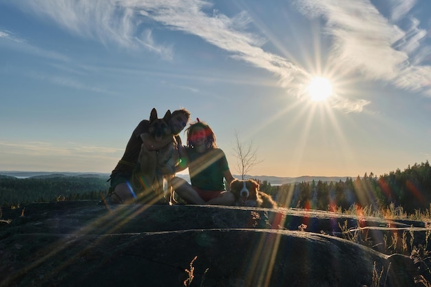 Jonge man en vrouw zitten op een rots en knuffelen hun honden Duitse en Australische herders