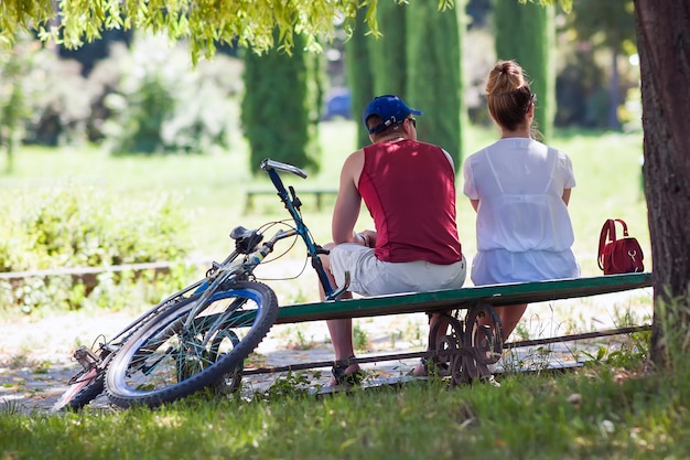 Jonge man en vrouwen die op een bank in park in de zonnige zomer zitten