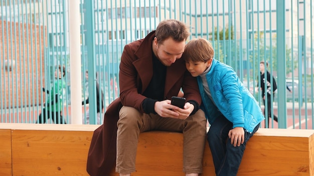 Jonge man en zijn kleine broertje zitten op de bank en kijken naar het scherm van de telefoon