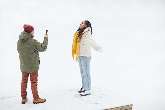 Jonge man fotografeert zijn vriendin op zijn mobiele telefoon terwijl ze poseren tijdens sneeuwweer