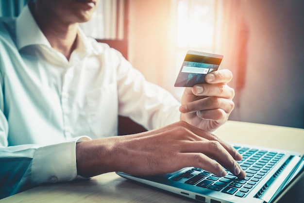 Jonge man gebruikt creditcard om online te winkelen op een laptopcomputertoepassing of website. E-commerce en online winkelconcept.