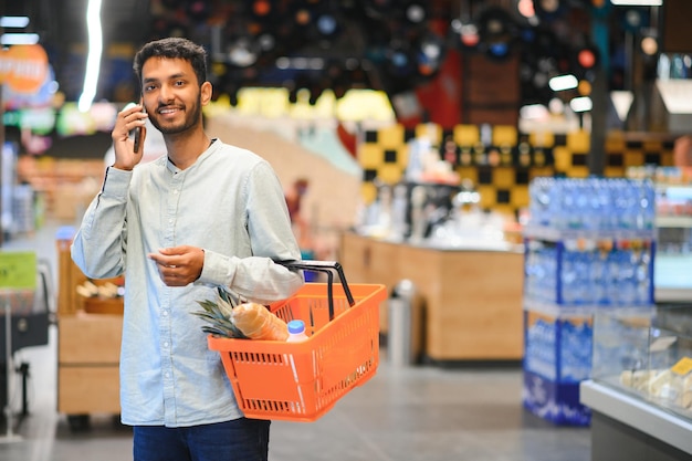 Jonge man gebruikt mobiele telefoon tijdens het winkelen in de supermarkt