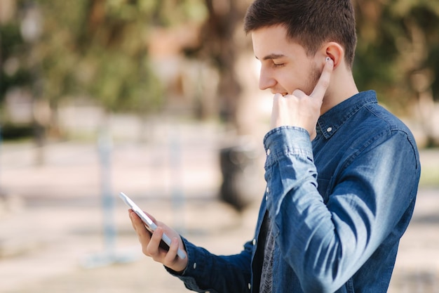 Jonge man gebruikt telefoon en draadloze koptelefoon en print bericht in sociaal netwerk