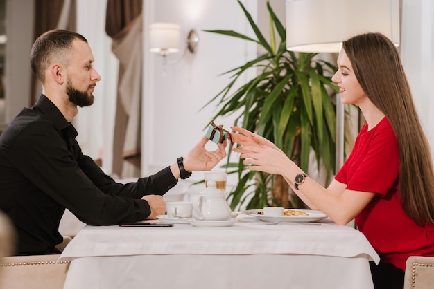 Jonge man geeft een doos met cadeau aan zijn vriendin in het restaurant