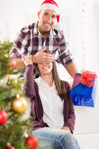 Jonge man geeft zijn vriendin een kerstcadeau met haar hand voor haar ogen.