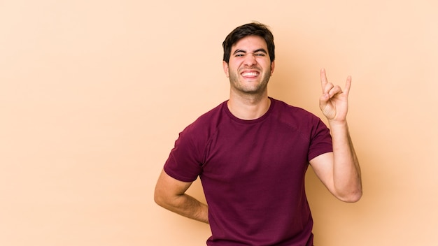 Jonge man geïsoleerd op beige met rock gebaar met vingers