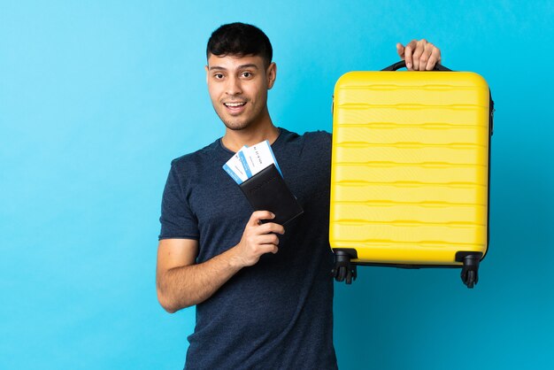 Jonge man geïsoleerd op blauw in vakantie met koffer en paspoort