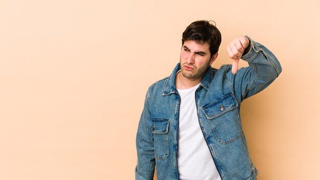 Jonge man geïsoleerd op een beige achtergrond met duim naar beneden en afkeer uiten.