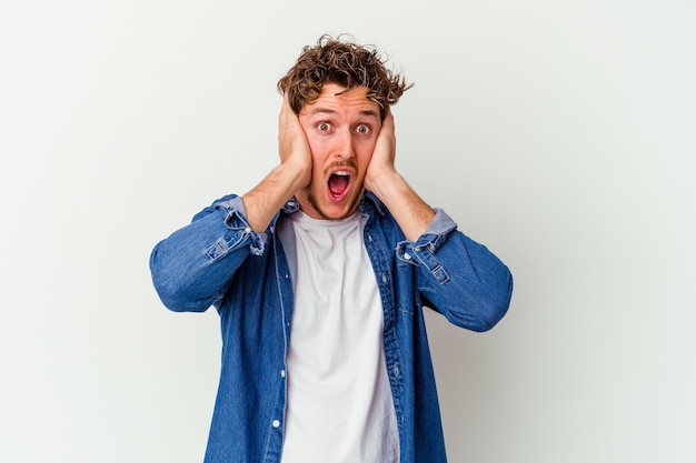 Jonge man geïsoleerd op een witte muur die oren bedekt met handen die niet te hard geluid proberen te horen