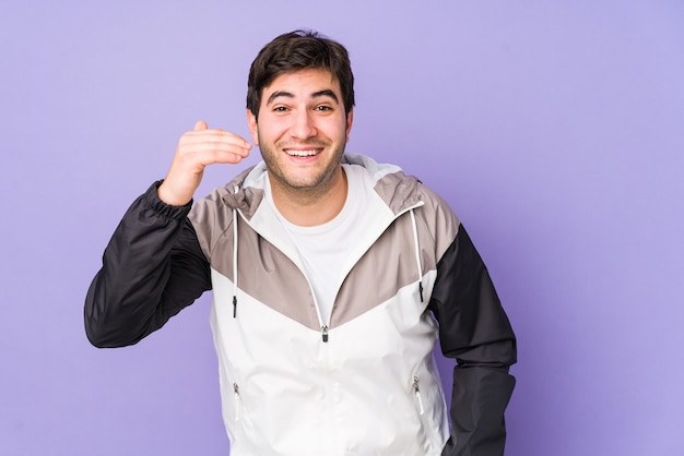 Jonge man geïsoleerd op paarse muur lachen om iets, mond bedekken met handen