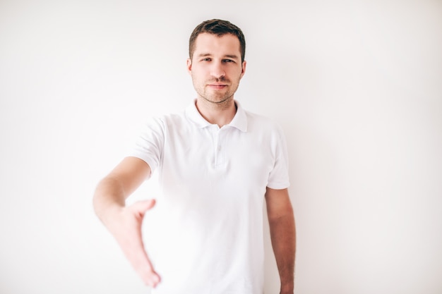 Jonge man geïsoleerd over witte muur. Kerel hield zijn hand recht om te schudden.