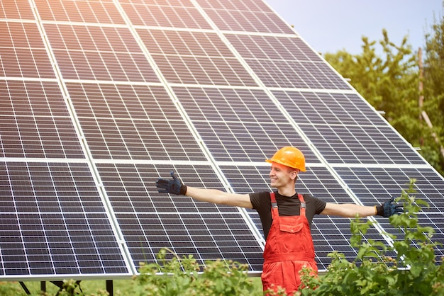 Jonge man glimlacht met open armen tegen de achtergrond van zonnepanelen, hij bevredigde zijn werk