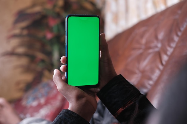 Jonge man hand met behulp van slimme telefoon met groen scherm liggend op de bank