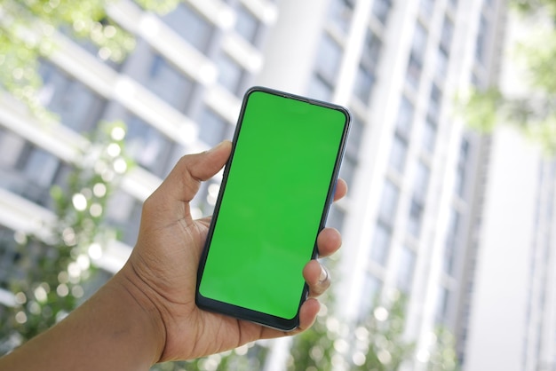 Jonge man hand met behulp van slimme telefoon met groen scherm tegen stadsgebouwen