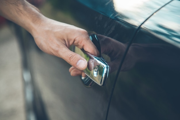 Jonge man hand op zwarte autodeur