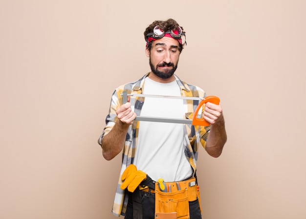 Jonge man huishoudster met een zaag op een vlakke muur