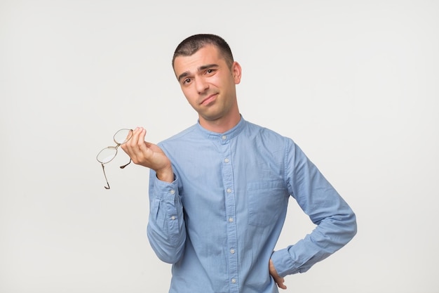 Jonge man in blauw shirt staande gedesoriënteerd verbijsterd geïsoleerd op grijze muur achtergrond Besluitvorming concept