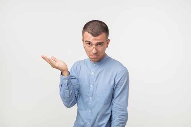 Jonge man in blauw shirt staande gedesoriënteerd verbijsterd geïsoleerd op grijze muur achtergrond besluitvorming concept