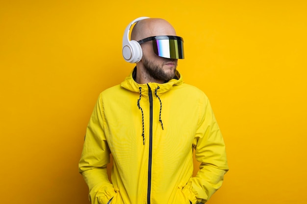 Jonge man in cyberpunk-bril in een gele jas met koptelefoon op een gele achtergrond