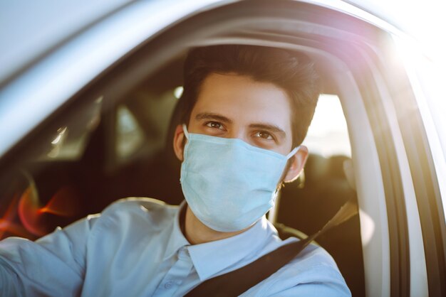 Jonge man in een beschermend masker in de auto zitten