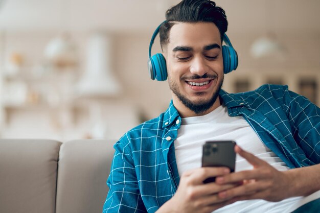 Jonge man in een blauwe t-shirt met een telefoon in handen zittend op de bank