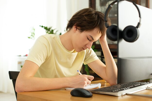 jonge man in een geel t-shirt werkt thuis op de computer. online chatten. werken op afstand via internet op isolatie