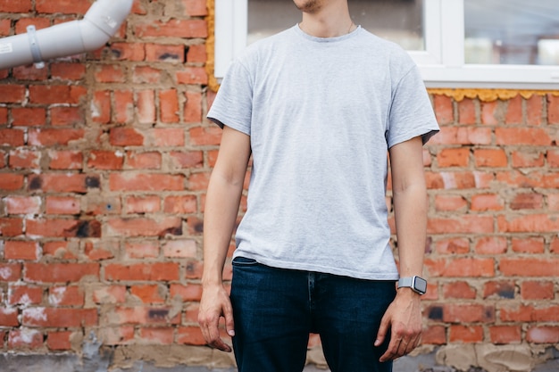 Jonge man in een grijs shirt en spijkerbroek poseren