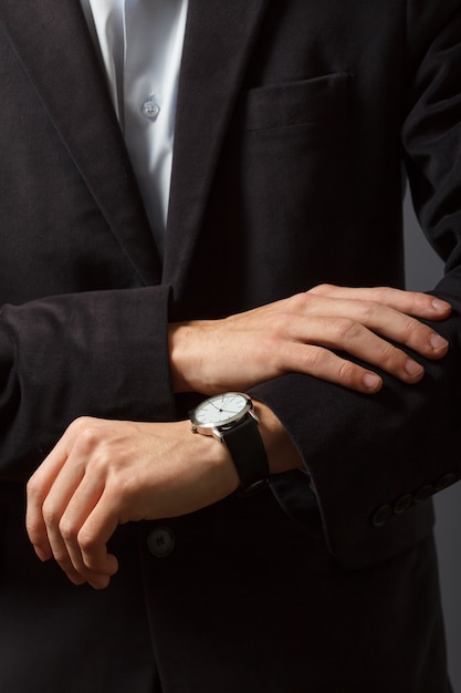 Jonge man in een pak staat en kijkt op zijn horloge