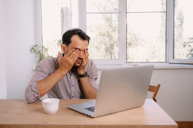 Jonge man in een shirt thuis bezig met een laptop