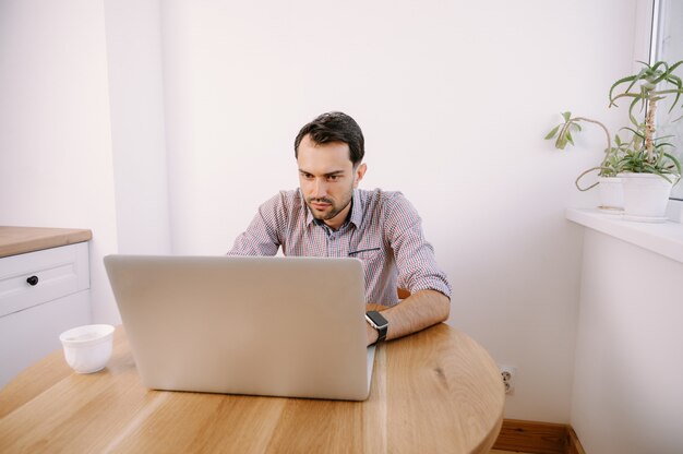 Jonge man in een shirt thuis bezig met een laptop