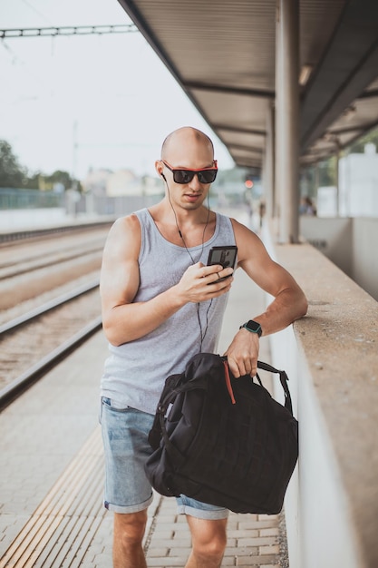 Jonge man in een t-shirt op het perron wachtend op een trein met behulp van mobiele telefoon man door treinstation pl