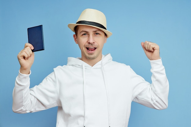 Jonge man in een witte trui met een hoed en paspoort