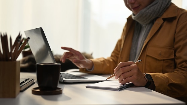 Jonge man in gele jas online werken met laptop thuis.