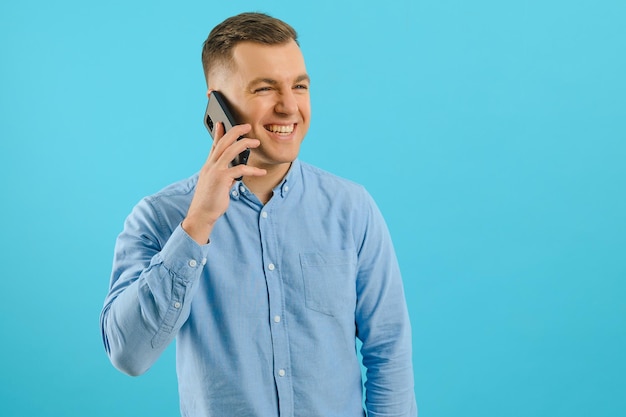 Jonge man in heldere kleurrijke slijtage praten op mobiele telefoon op blauwe achtergrond. Trendy man heeft een gesprek. Smartphone, technologieconcept.