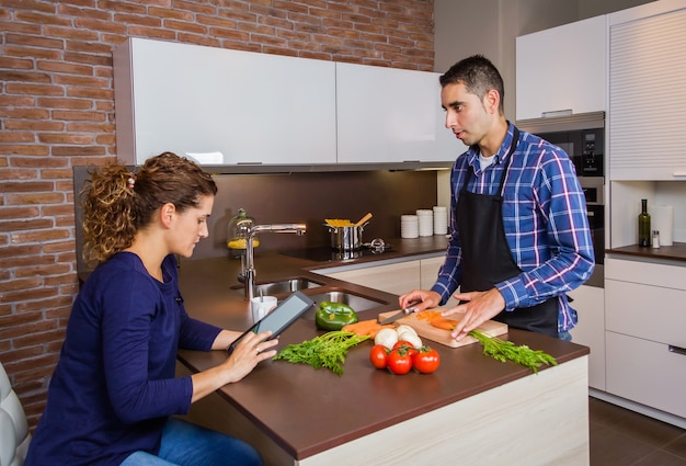Jonge man in huis keuken bereiden van voedsel en vrouw op zoek recept in een elektronische tablet. Modern gezinslevensstijlconcept.