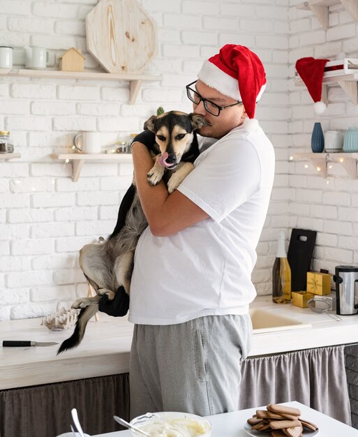 Jonge man in kerstmuts met zijn hond in zijn armen in de keuken