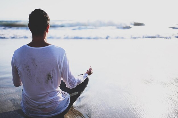 Foto jonge man in meditatie bij de zee concept van bidden volwassenen beoefenen yoga op het strand bij zonsondergang