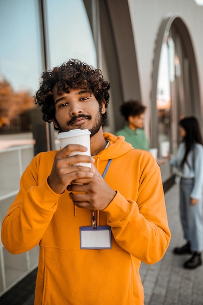 Jonge man in oranje hoodie met een beker zonder morsen in handen