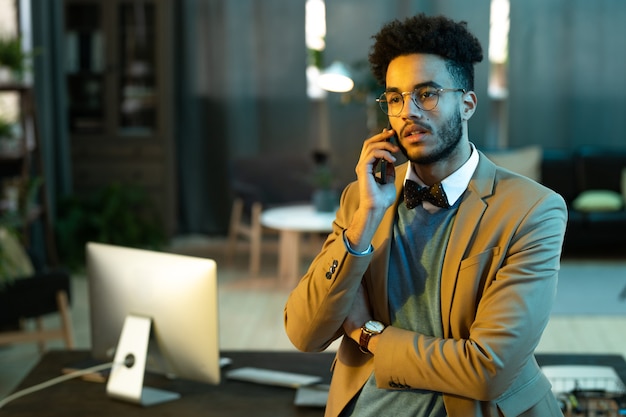 Jonge man in pak heeft een gesprek op zijn mobiele telefoon terwijl hij op kantoor werkt