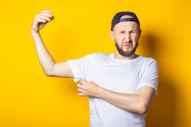 Foto jonge man in pet en t-shirt met zweterige en stinkende oksels op gele achtergrond.