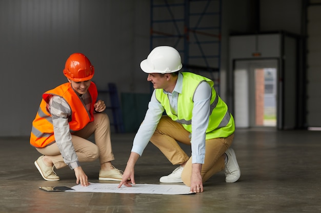 Jonge man in reflecterende kleding project van nieuw gebouw bespreken samen met zijn collega terwijl ze in een leeg gebouw zijn