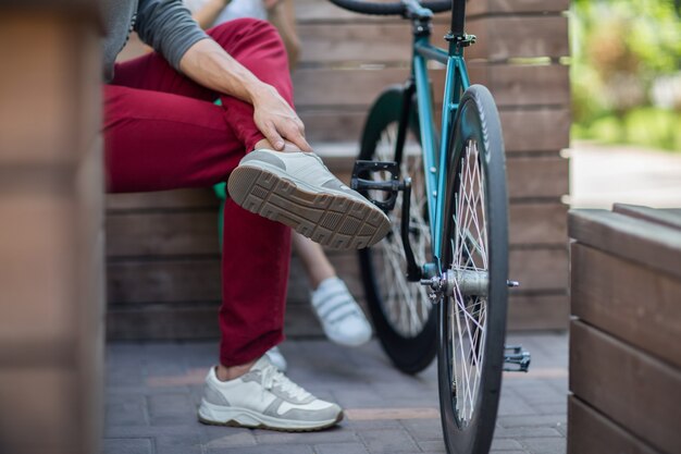 Jonge man in rode broek rust in een park op een bankje na een ritje op de baanfiets.