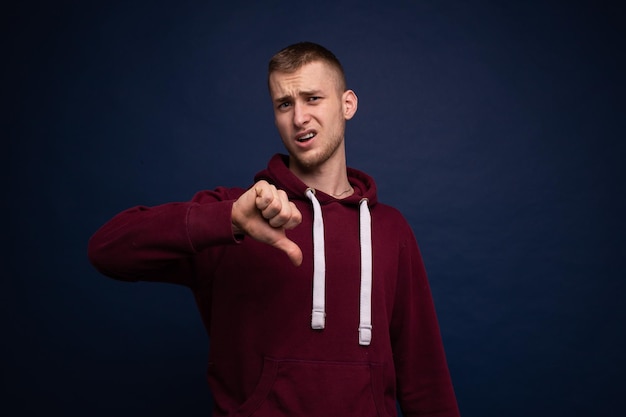 Jonge man in rode hoodie en spijkerbroek poseren op blauwe achtergrond, nederlaag tonen