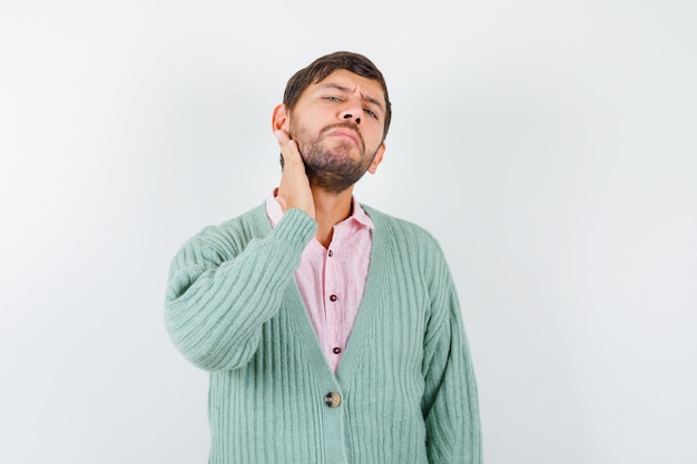 Jonge man in shirt, vest die gezichtshuid controleert door baard aan te raken en peinzend, vooraanzicht te kijken.